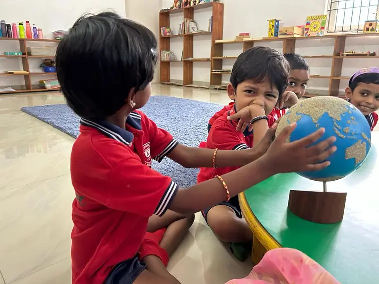 A KIMS child smiling as she spins a Montessori globe